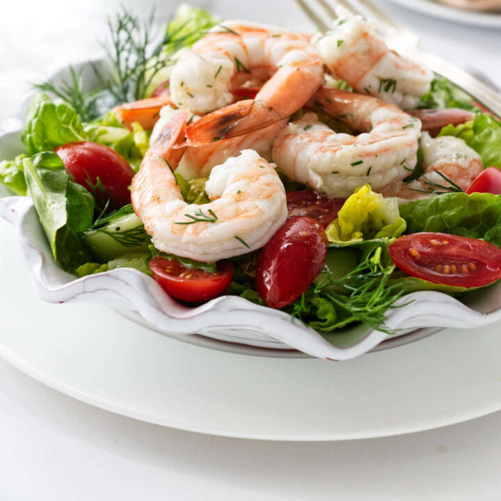 A lettuce salad with shrimp, tomatoes, and cucumbers.