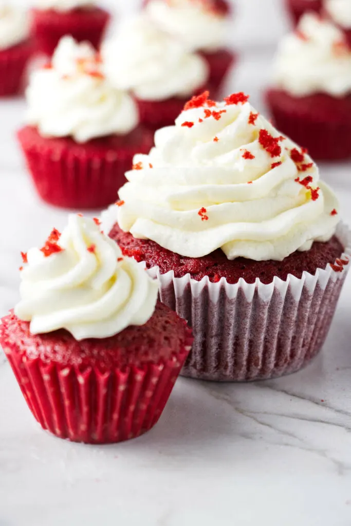 A mini red velvet cupcake next to a standard sized cupcake.