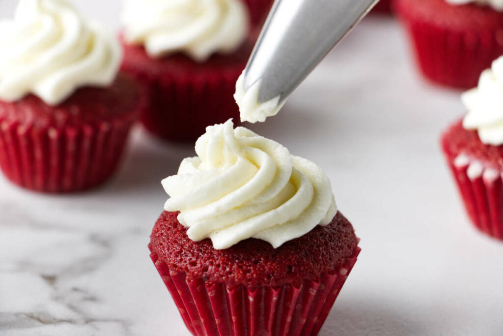 Piping cream cheese frosting on a red velvet mini cupcake.