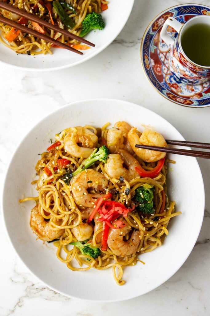 A bowl filled with shrimp yakisoba and a cup of green tea.