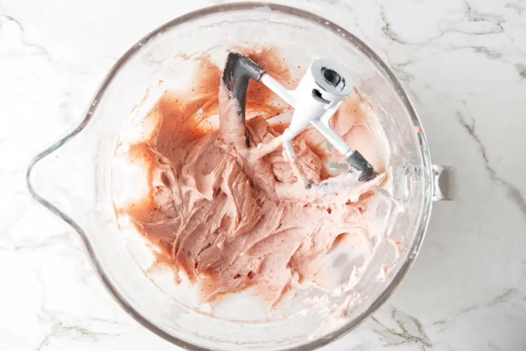 Beating the cream cheese until the strawberry frosting is smooth and creamy.