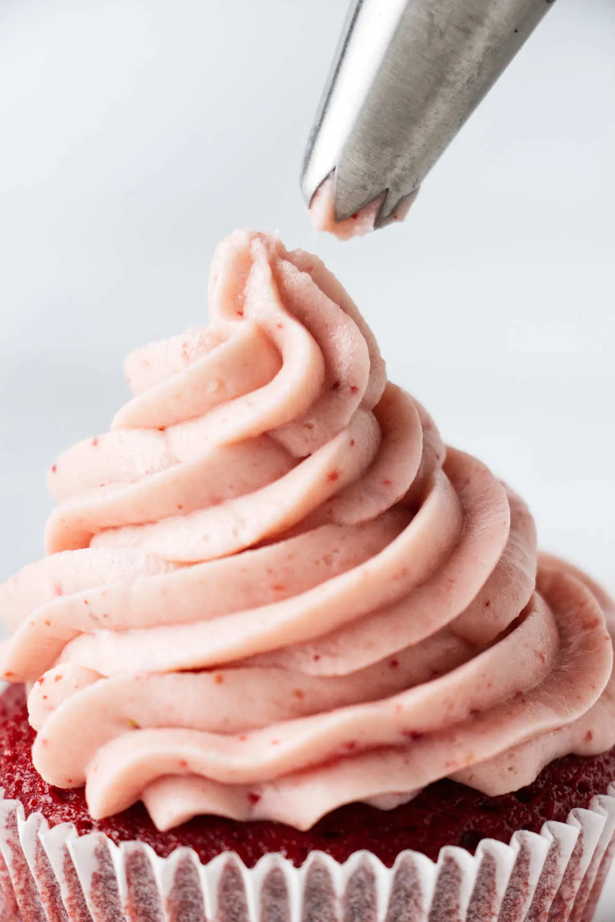 Piping strawberry frosting on a cupcake.