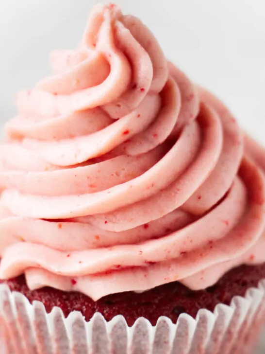 A cupcake topped with strawberry cream cheese frosting.