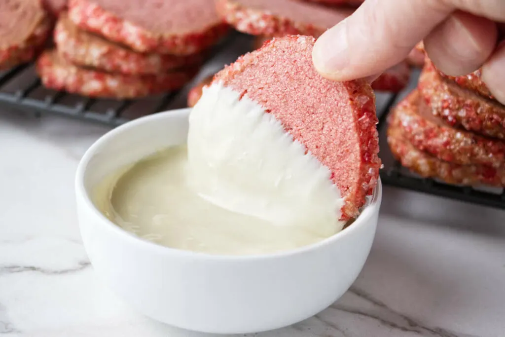 Dipping a strawberry shortbread cookie in melted white chocolate.