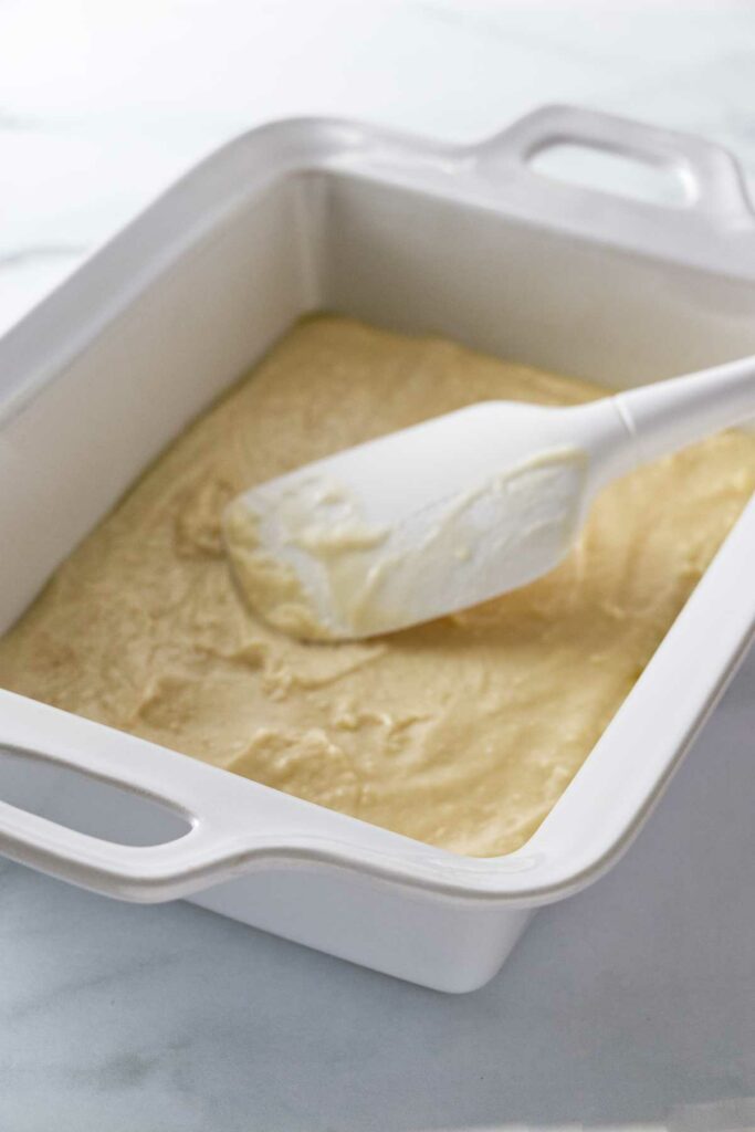 Cake batter and spatula being spread into the baking dish.