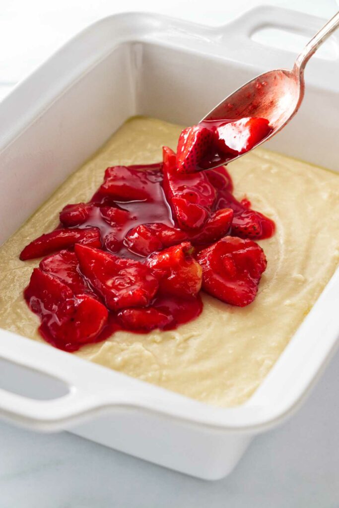 Strawberries being spooned over the top of the cake batter.