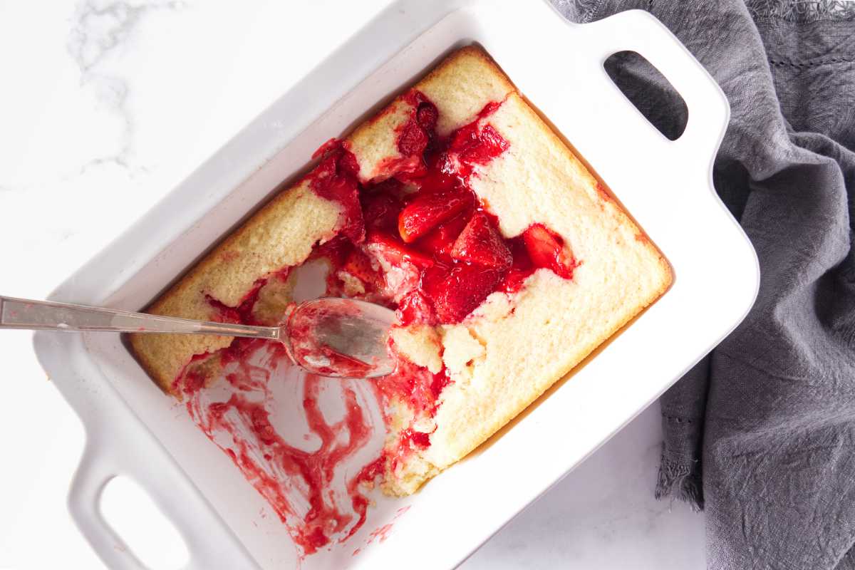 Overhead view of a dish of strawberry cake with a serving spoon.