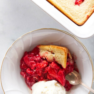 A serving of strawberry spoon cake with a scoop of vanilla ice cream. The dish of spoon cake next to the serving.