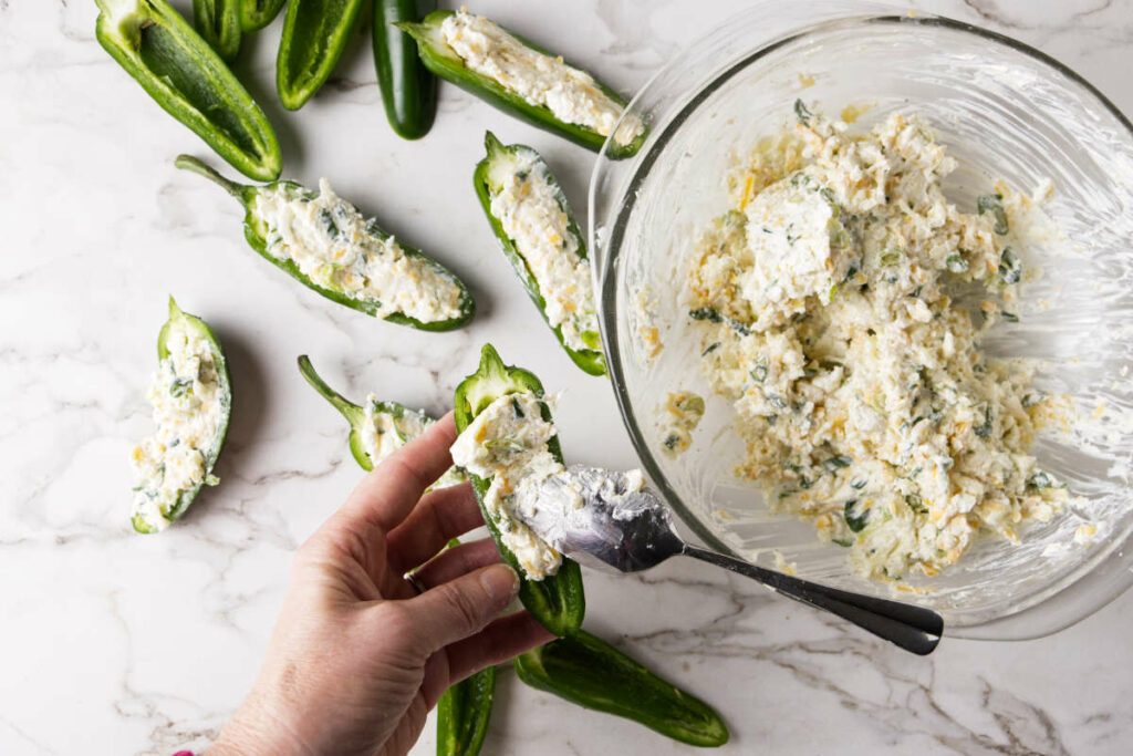 Spooning a cheese mixture inside jalapeños.