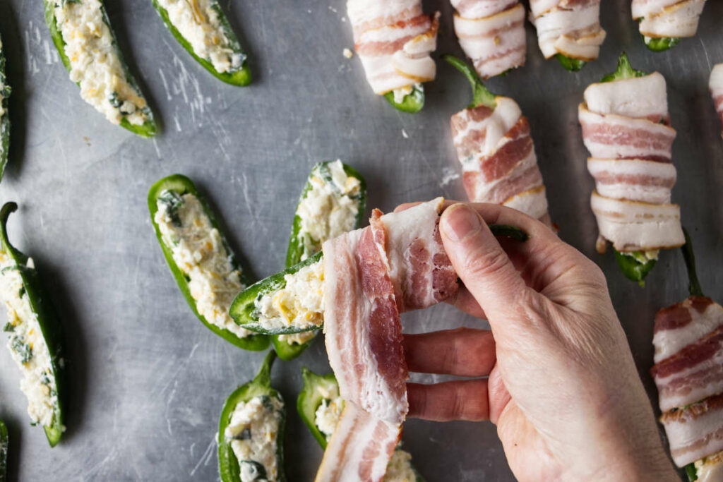 Wrapping bacon around a stuffed jalapeno.