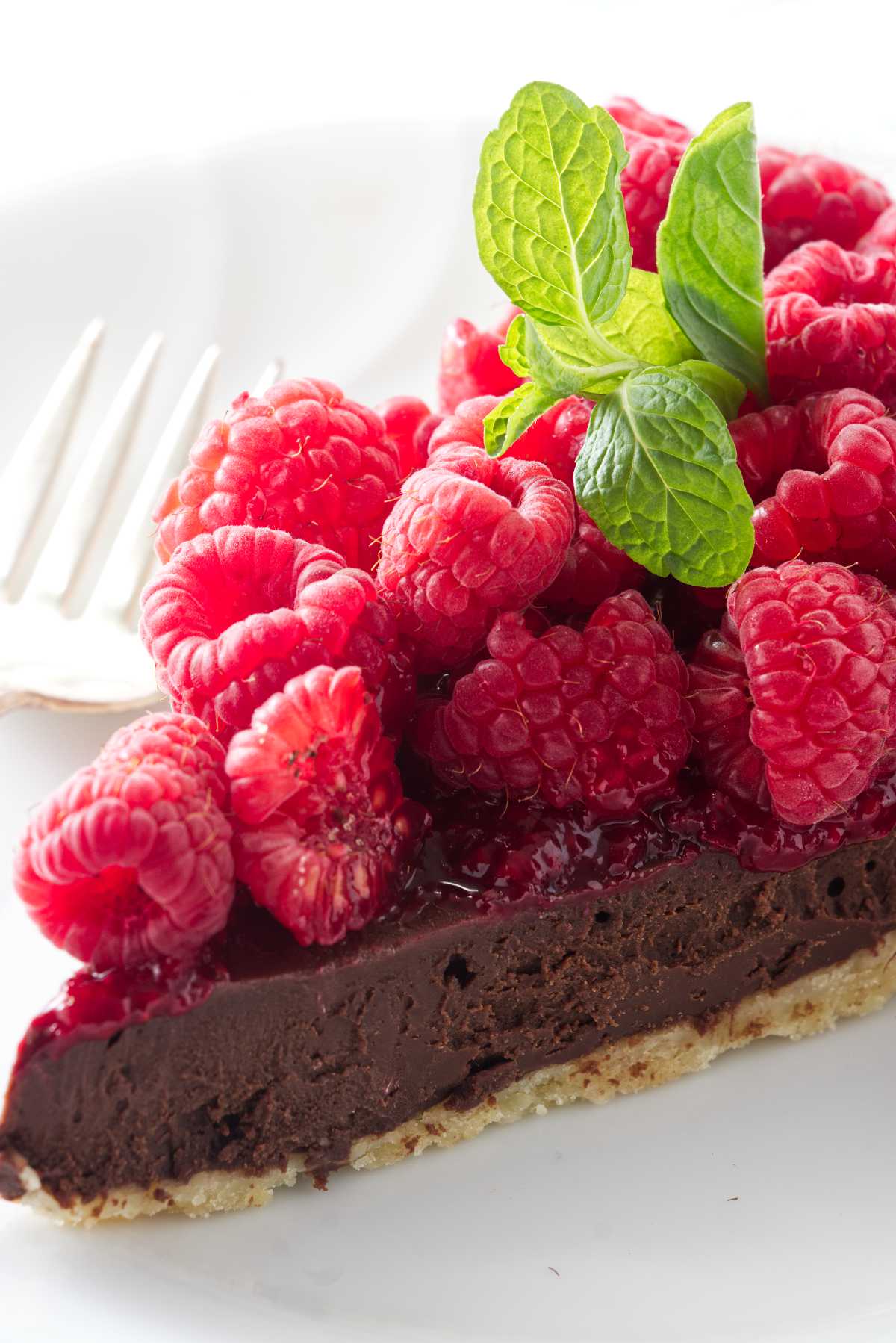 A slice of a chocolate tart topped with raspberries and raspberry sauce.