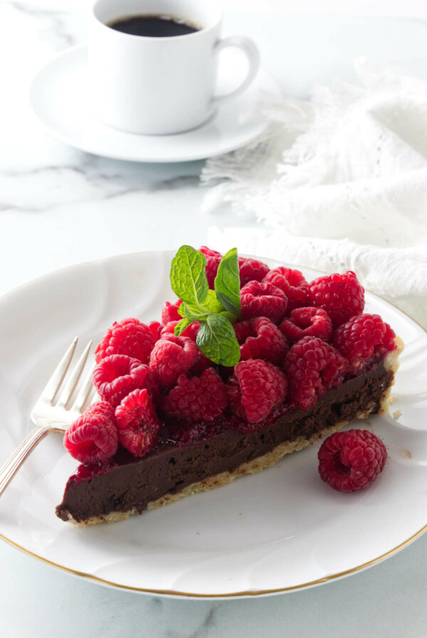 A slice of a tart on a dessert plate next to a cup of coffee.