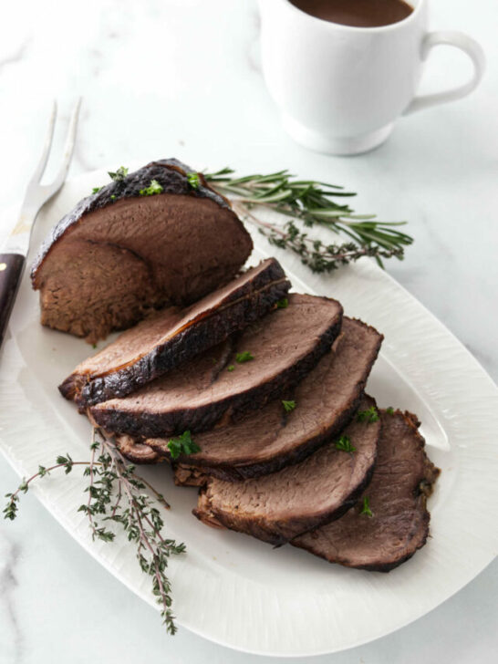 A sliced sirloin tip roast next to a pitcher of gravy.