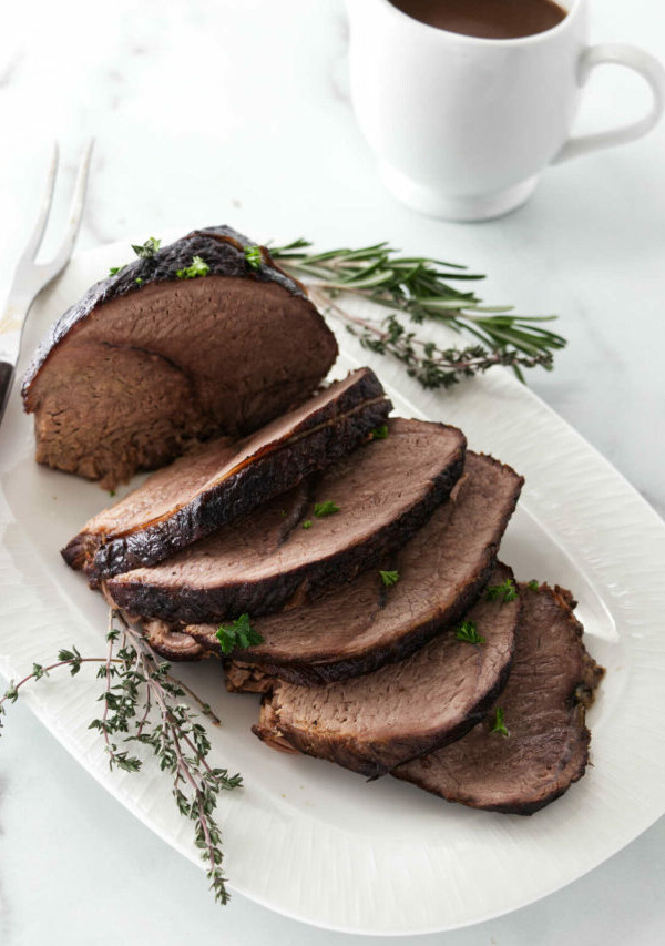 A sliced sirloin tip roast next to a pitcher of gravy.