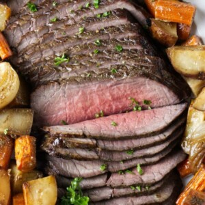 Thinly sliced beef on a platter with roasted veggies.