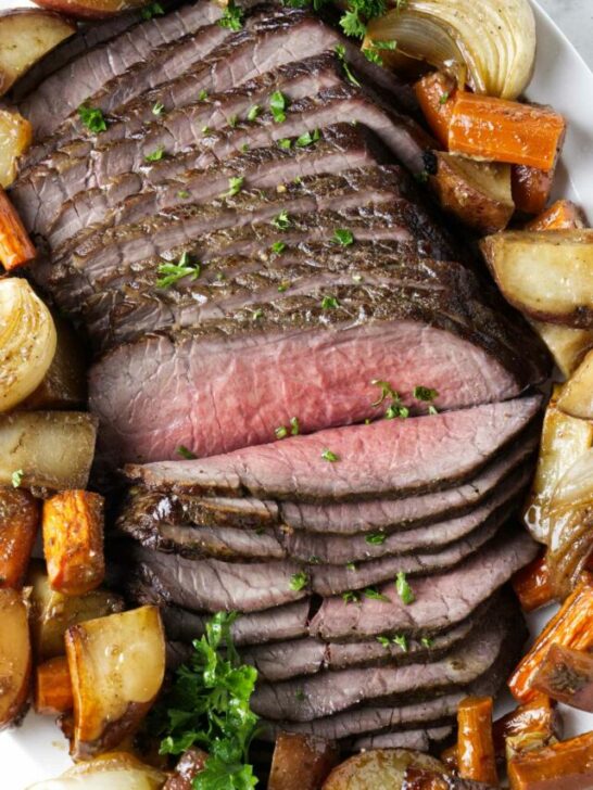 Thinly sliced beef on a platter with roasted veggies.