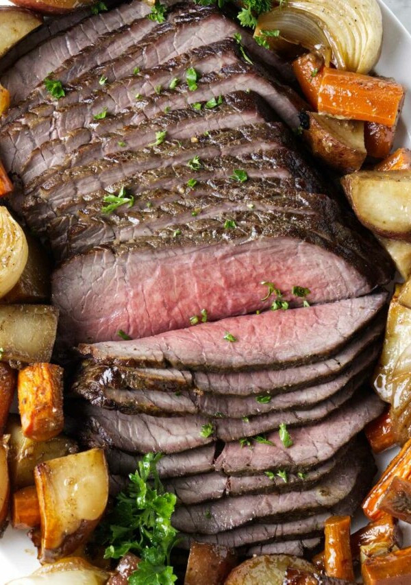 Thinly sliced beef on a platter with roasted veggies.