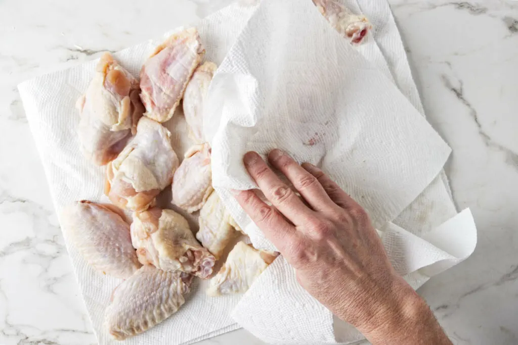 Patting the chicken wings dry with paper towels.