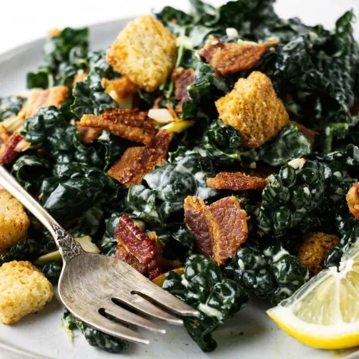 A lemon kale caesar salad on a plate with bacon and croutons.