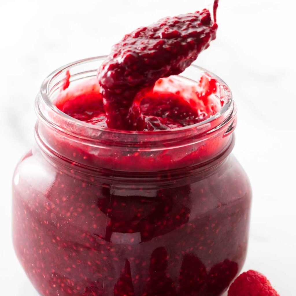 Spooning raspberry sauce out of a jar.
