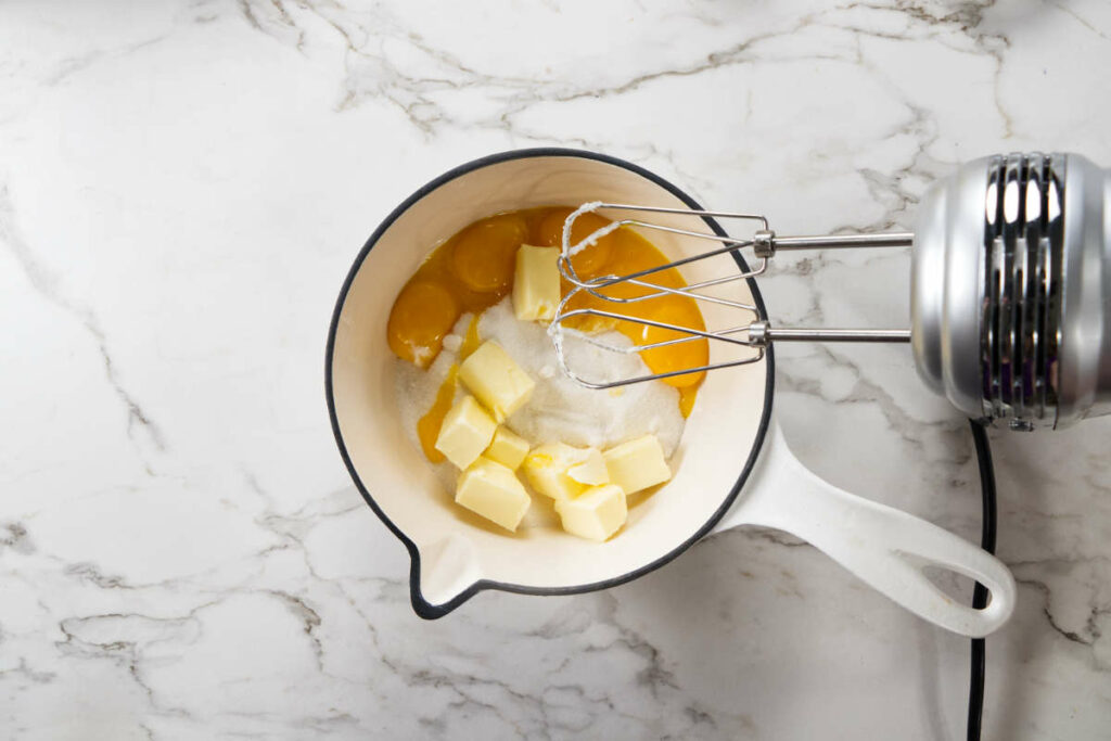 Adding egg yolks to butter and sugar in a saucepan.