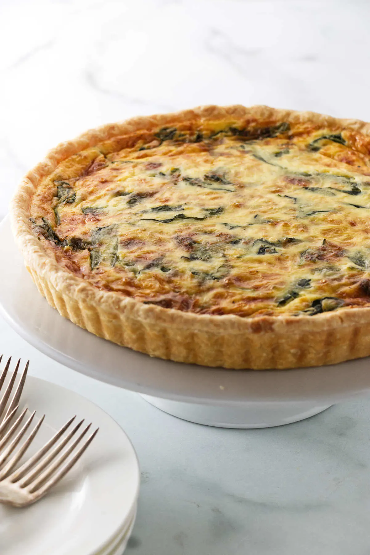 A quiche on a serving platter next to dinner plates.