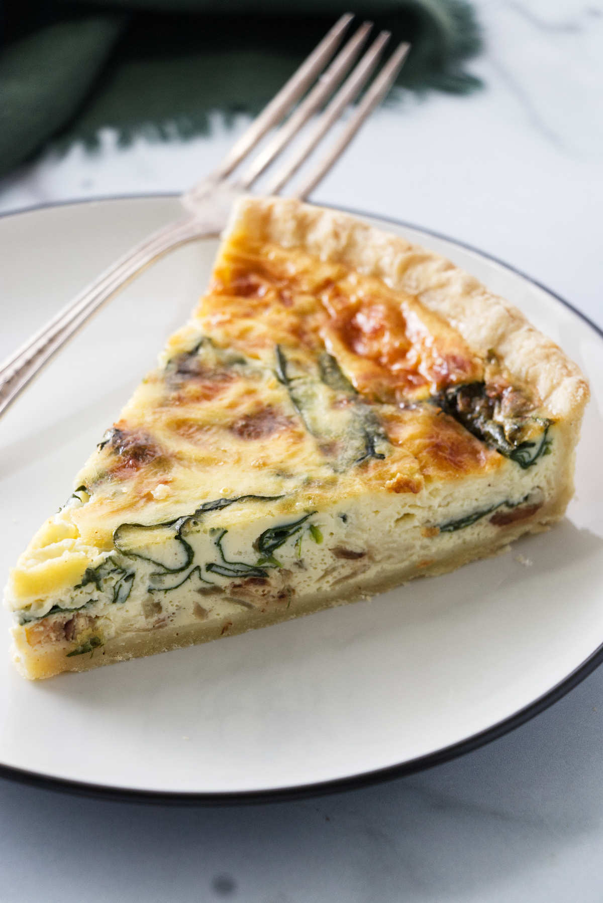 A slice of quiche with spinach baked into the center of the quiche.