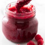 Scooping raspberry sauce out of a jar.
