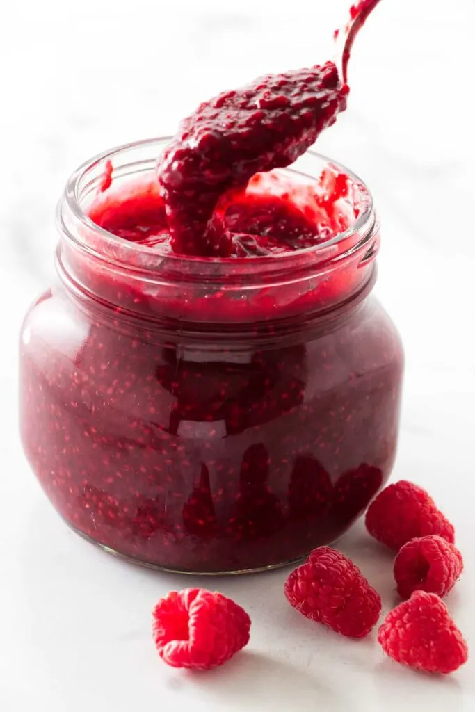 Scooping raspberry sauce out of a jar.