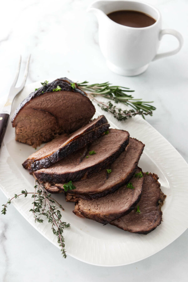 A sliced sirloin tip roast next to a pitcher of gravy.