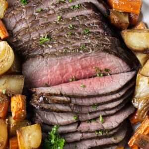 Thinly sliced beef on a platter with roasted veggies.