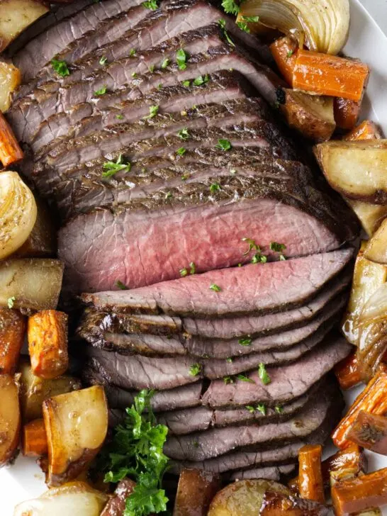 Thinly sliced beef on a platter with roasted veggies.