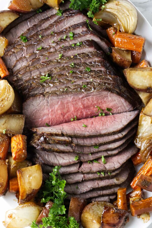 Thinly sliced beef on a platter with roasted veggies.