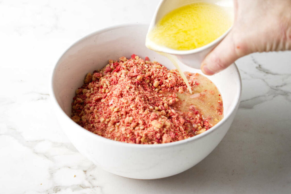 Mixing butter into a bowl with strawberry shortcake crumble.