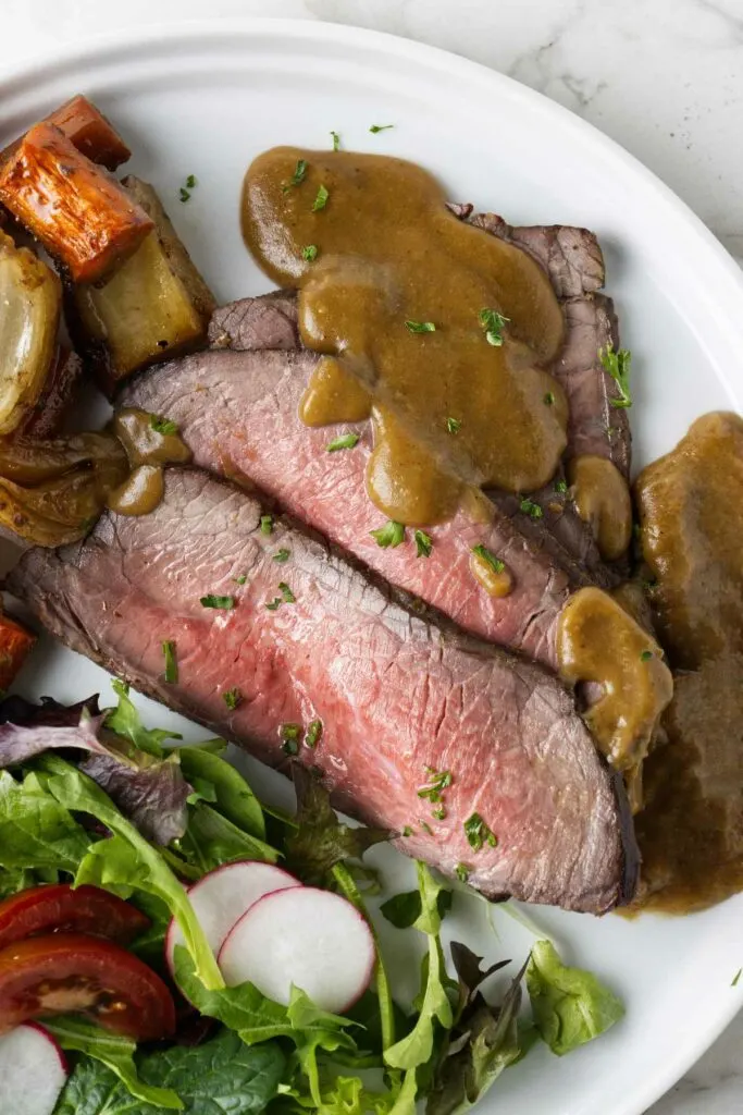 Slices of London broil on a platter with gravy and vegetables.