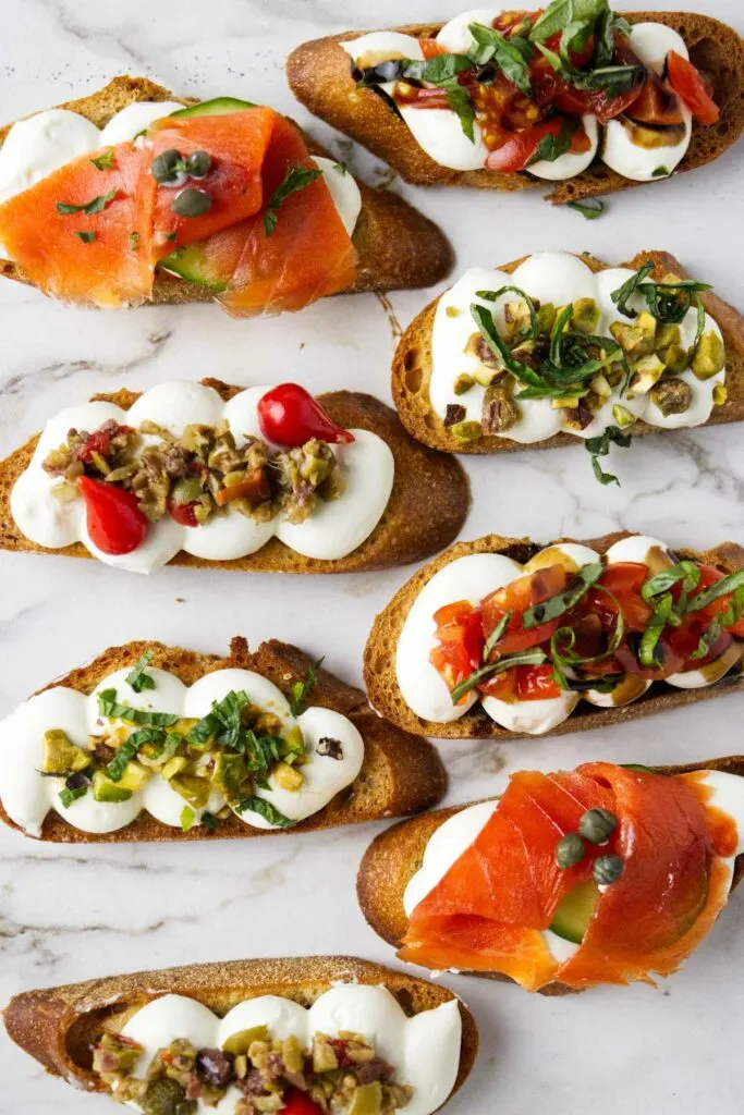 Several whipped ricotta crostini with various toppings like smoked salmon and tomatoes.