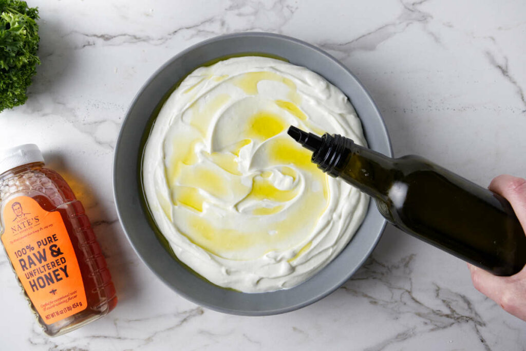Drizzling olive oil over a bowl of ricotta dip.