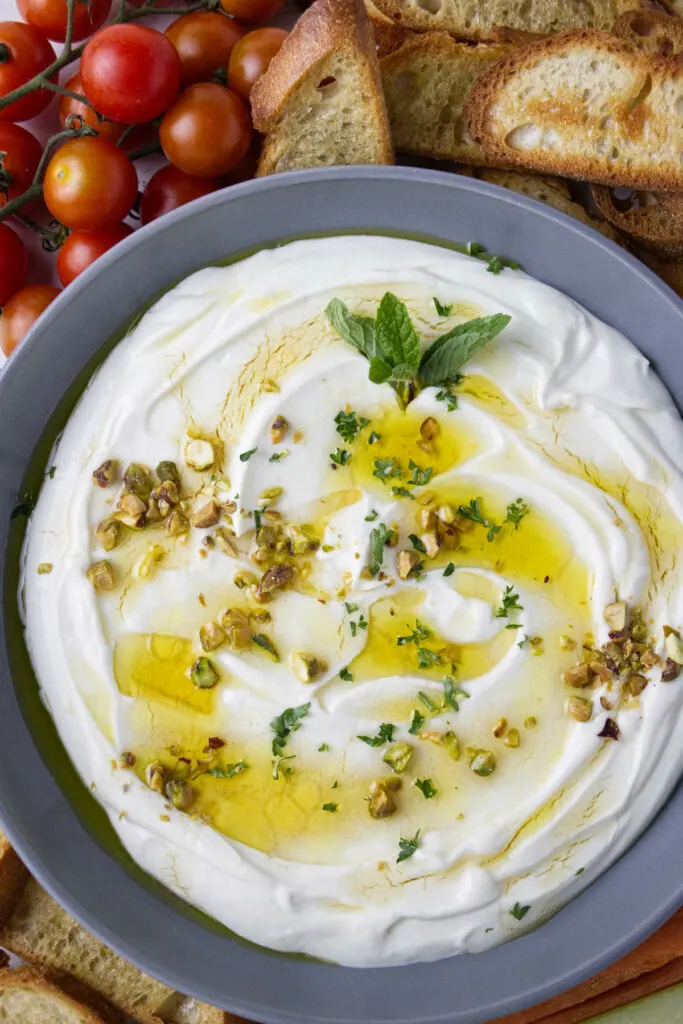 Crostini and tomatoes next to a bowl filled with whipped ricotta.