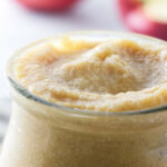 Apple curd in a jar next to apples.