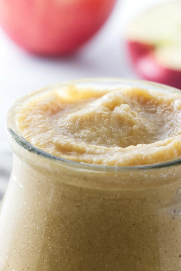 Apple curd in a jar next to apples.