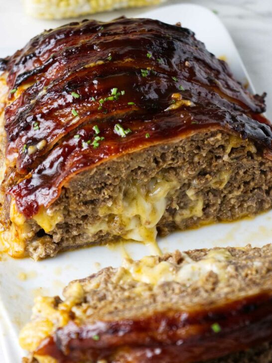 Bacon wrapped meatloaf stuffed with cheese on a serving platter.