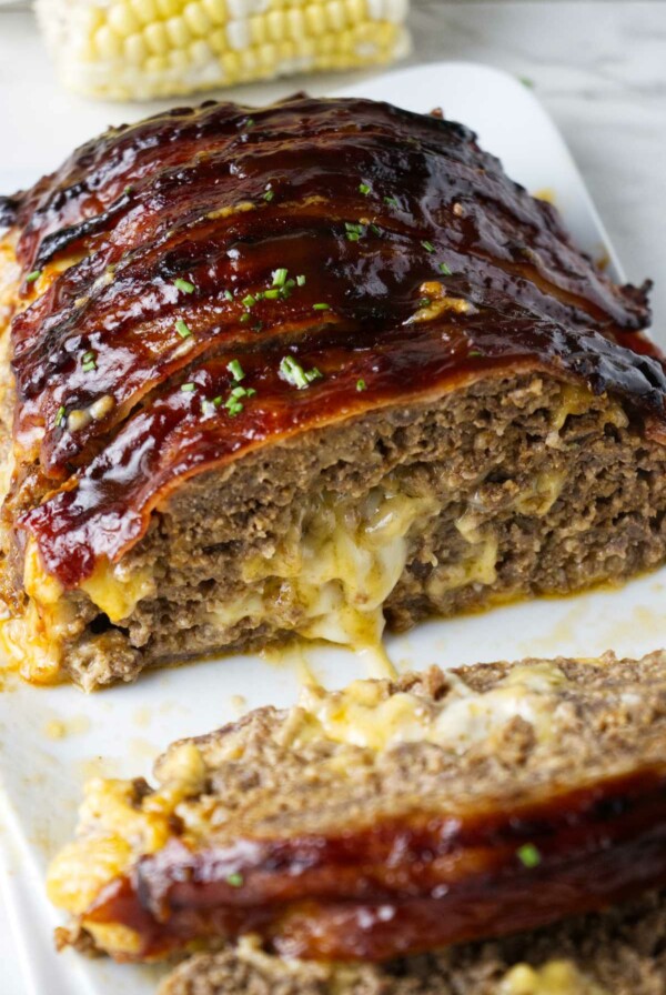 Bacon wrapped meatloaf stuffed with cheese on a serving platter.