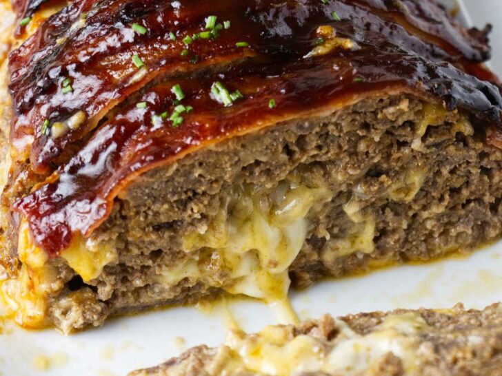 Bacon wrapped meatloaf stuffed with cheese on a serving platter.