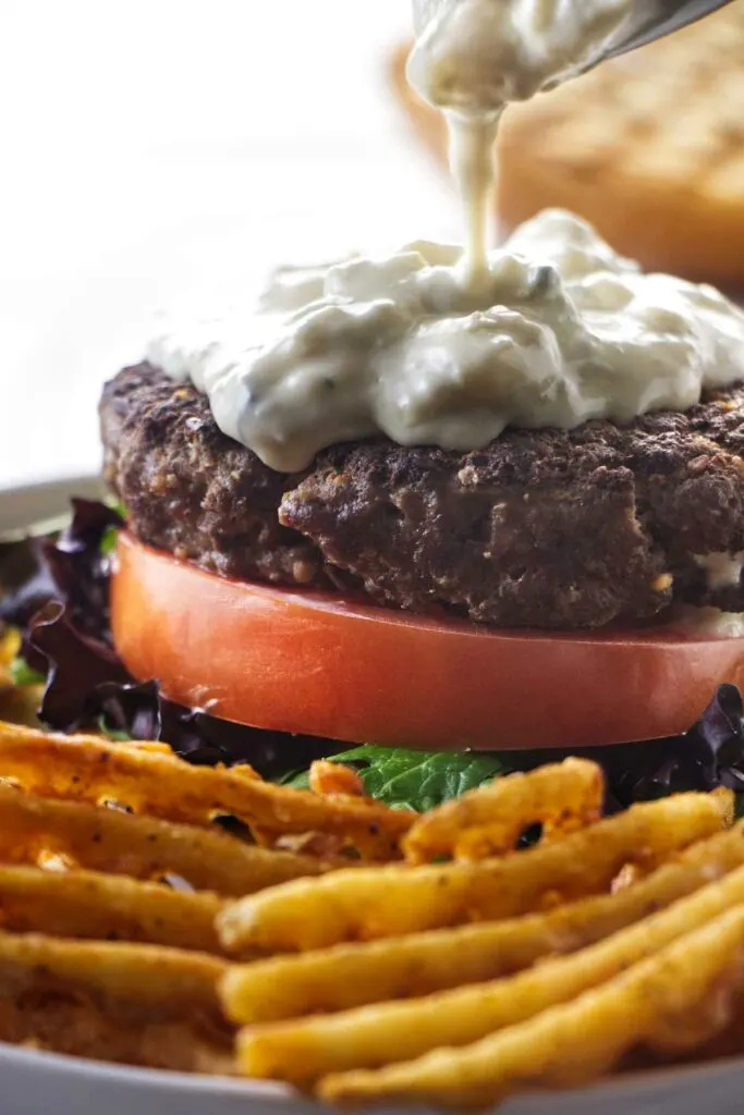 Drizzling blue cheese sauce on a steak burger.