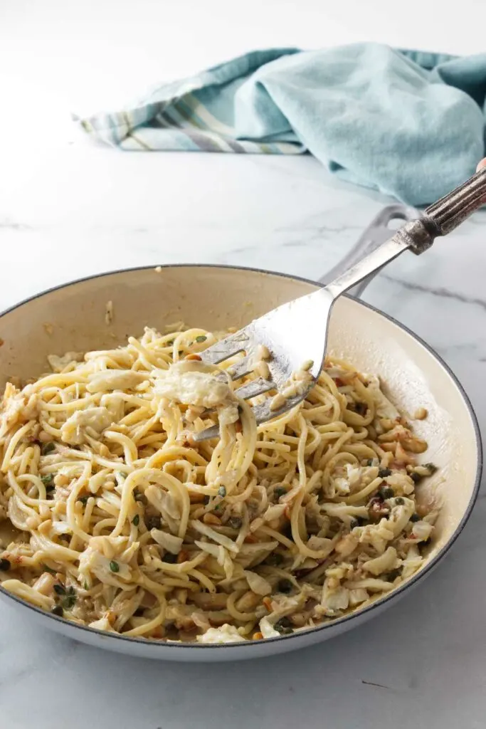 A large serving fork tossing the crabmeat in the skillet of pasta.