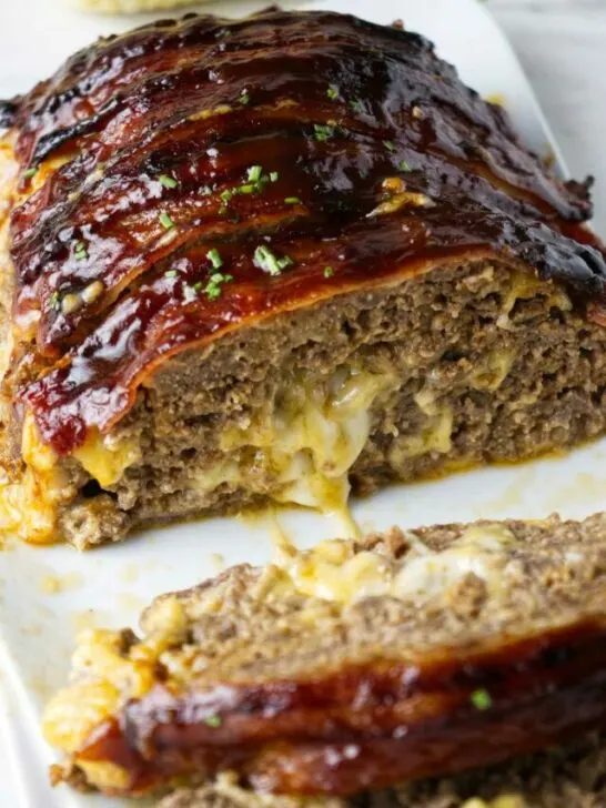 Bacon wrapped meatloaf stuffed with cheese on a serving platter.