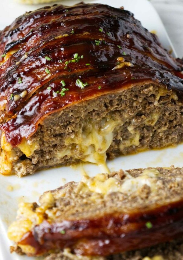 Bacon wrapped meatloaf stuffed with cheese on a serving platter.