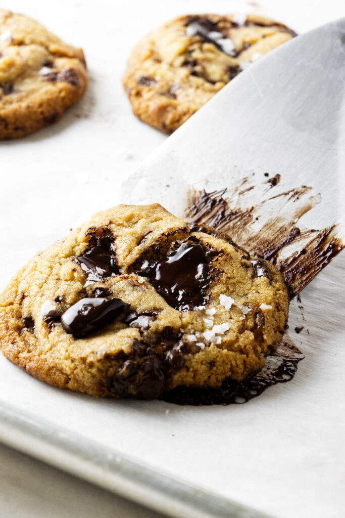 Using a spatula to scoop a cookie off a baking sheet.