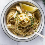 A serving of crab pasta with a wedged of lemon and a fork in it.