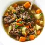 A bowl of oxtail soup with a spoon.